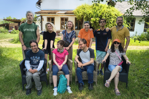 Klausur-Gruppen-Bild vor dem Haarberghof-Haus auf grüner Wiese mit sitzenden und dahinterstehenden Menschen in verschiedenfarbiger Kleidung und einigem Lächeln in verschiedene Richtung.