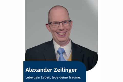 Porträtfoto eines lächelnden Mannes mit Brille im Anzug und Krawatte. Unten im Bild steht der Name Alexander Zeilinger und der Satz Lebe dein Leben, lebe deine Träume. auf einem blauen Hintergrund.