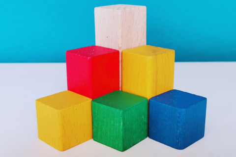 Türkis-weißer Hintergrund, zu einem Turm gestapelte Bausteine in verschiedenen Farben